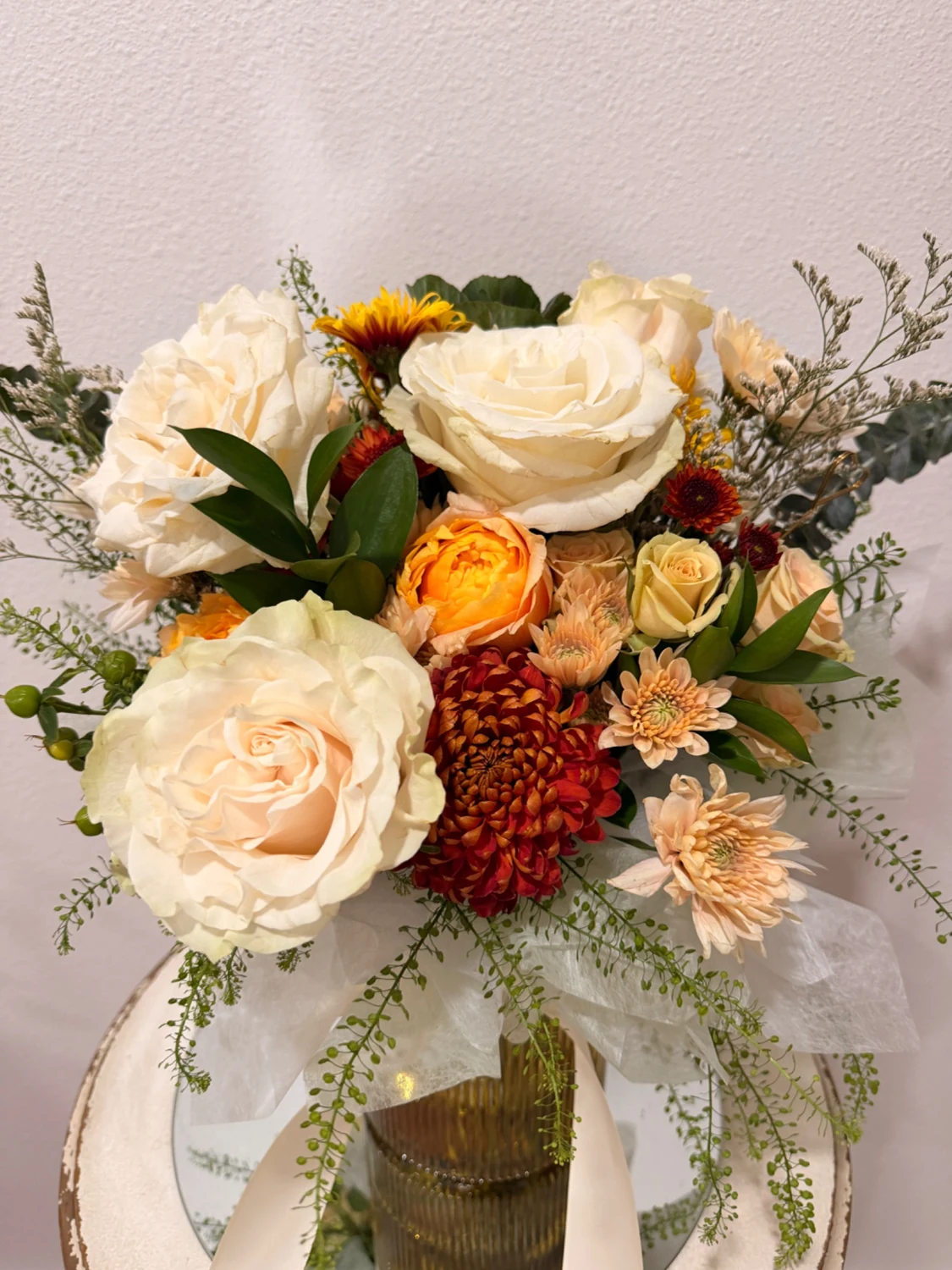Cream roses, warm orange flowers, and textured greenery